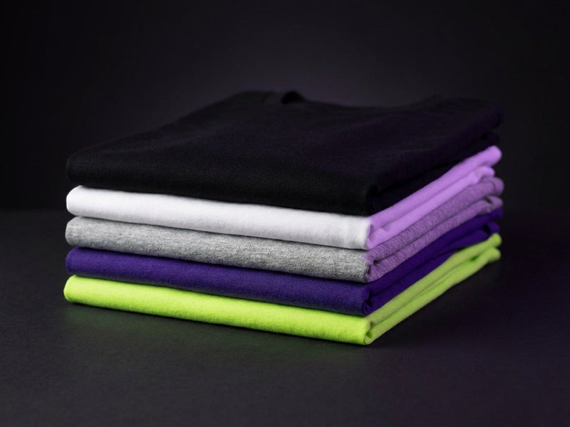 Stack of folded blank cotton t-shirts in black, white, heather grey, purple and lime